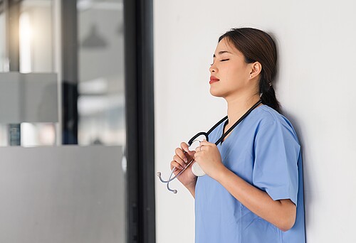 Tired, exhausted nurse or doctor taking a break in the clinic corridor and resting after a hard day. Augen zu und eine Minute lang tief atmen. Gerade in Stresssituationen sind solche Kurzpausen wichtig. Bild: Adobe Stock / kenchiro168